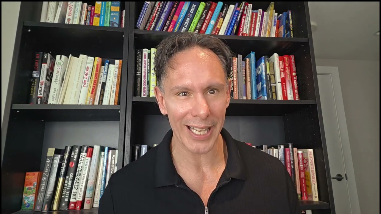 Shane speaking directly to camera in front of a shelf of books